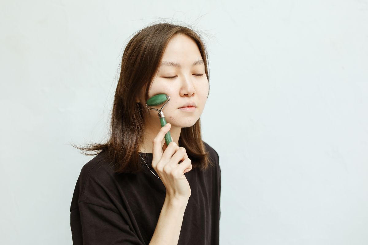 Woman using a jade facial roller, part of the Korean-inspired skincare ritual