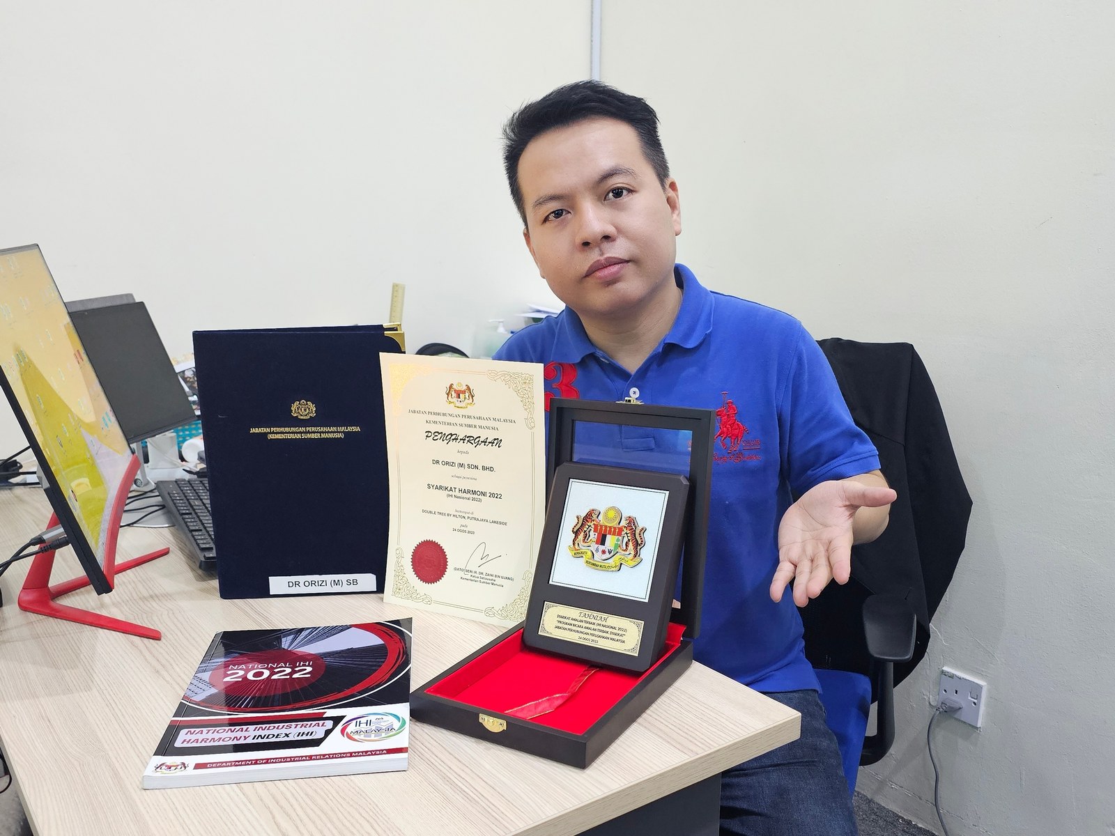 Dr Orizi representative presenting the Syarikat Harmoni 2022 certificate and medallion at his desk